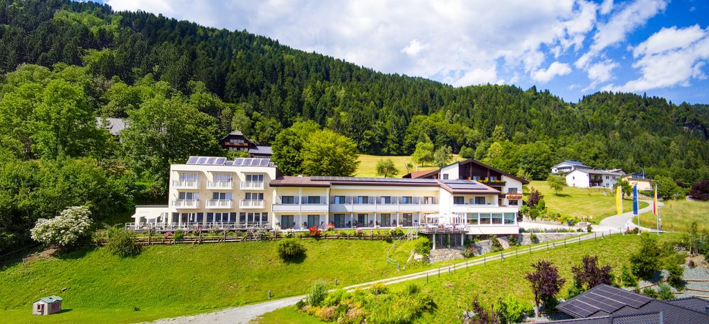 Das Hotel Ossiacher See von außen, am Hang über dem See mit Wald im Hintergrund